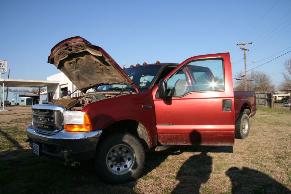 Red Ford F-350 truck, hood and driver door open, parked outside. Another truck is visible behind it