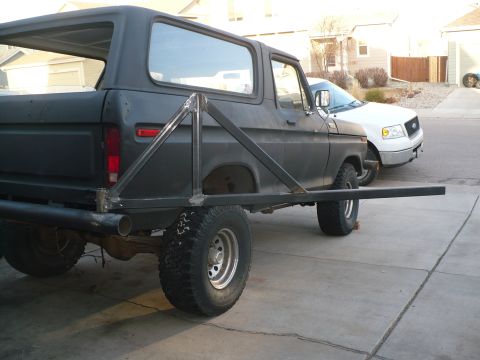 1979 Ford Bronco - The rear of a classic Ford Bronco is shown with a custom tire carrier, parked next to a white pickup truck.