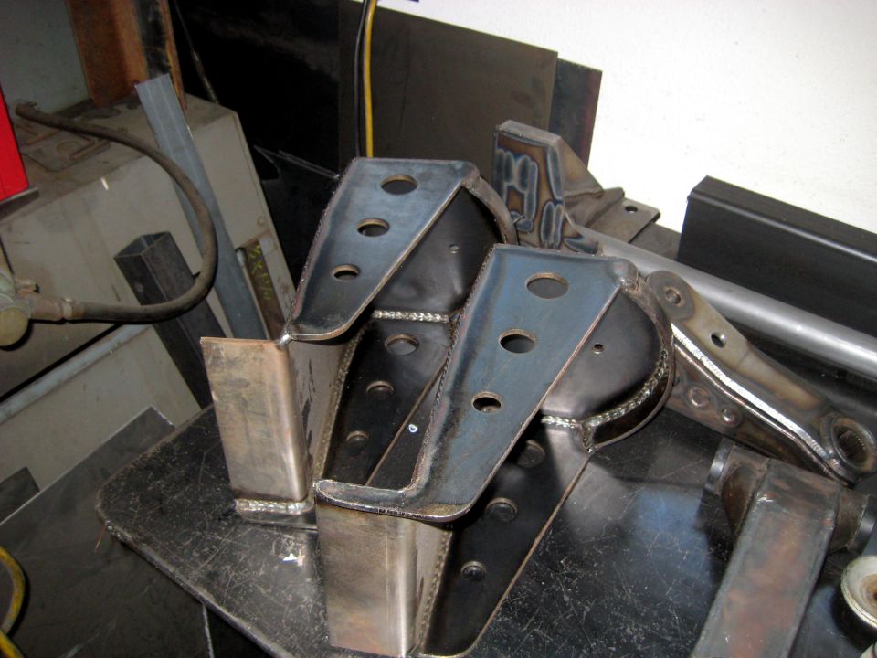 Two welded steel brackets with multiple holes, resting on a metal surface