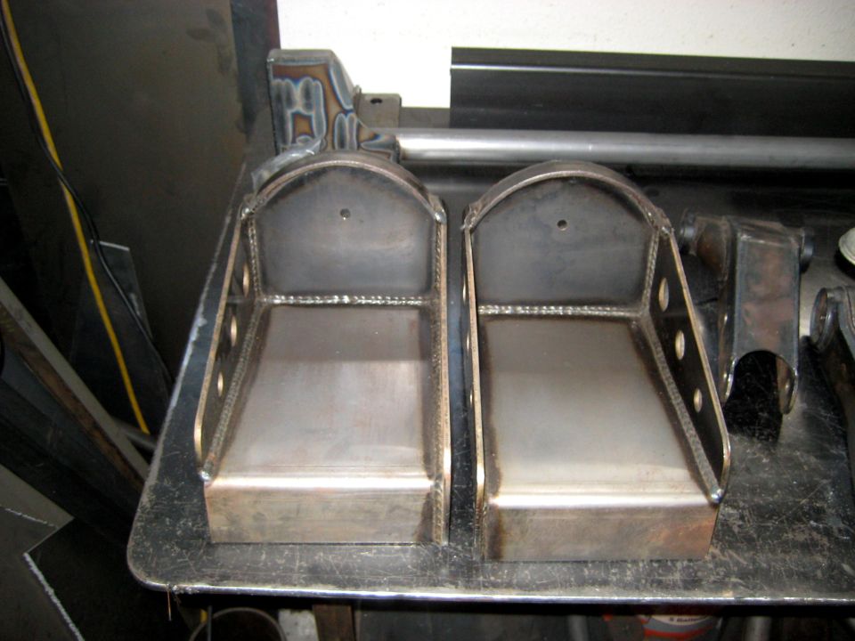 two fabricated metal brackets on a workbench