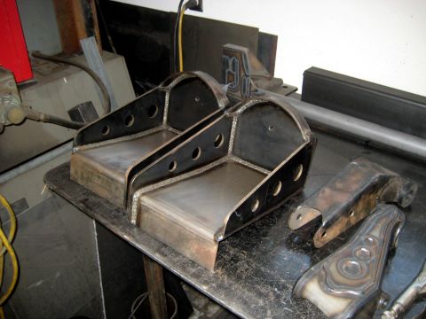 1996 Ford Bronco - Fabricated metal brackets and suspension components are laid out on a workbench, likely in a workshop setting.