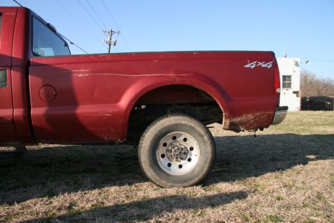 1993 Ford Bronco - Rear side view of a red pickup truck, showing the wheel well and a 4x4 decal on the bed.