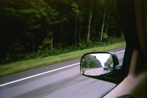 1985 Ford Bronco - A red car is visible in the side mirror of a vehicle driving on a highway.