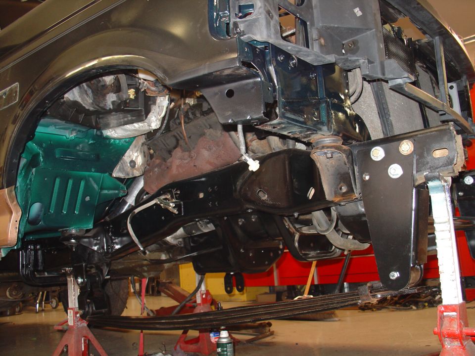 Underside of a disassembled SUV on jack stands showing frame, engine and teal inner fender