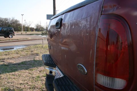 1993 Ford Bronco - Rear view of a dented red Ford pickup truck, with a Jeep in the background.