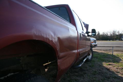 1993 Ford Bronco - A red pickup truck with visible body damage is parked next to another truck.