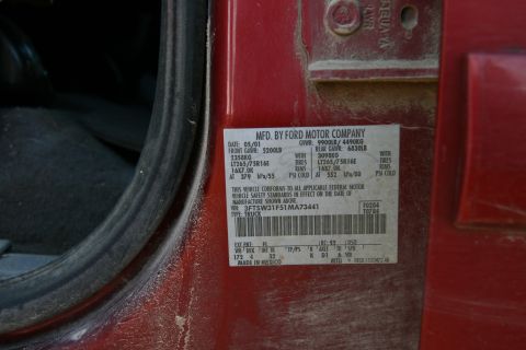 1993 Ford Bronco - A close-up of a red vehicle's door jamb reveals a sticker with manufacturing details and VIN.