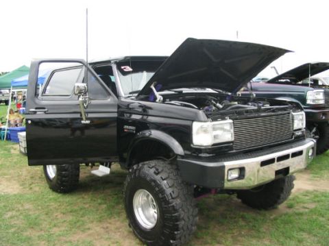 1994 Ford Bronco - Black Ford Bronco with hood open and door ajar, parked on grass next to another vehicle.