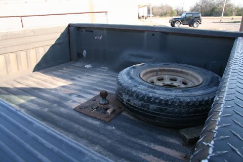 1993 Ford Bronco - The bed of a pickup truck contains a spare tire and a fifth wheel hitch, with another vehicle visible in the distance.