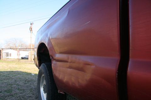 1993 Ford Bronco - A red pickup truck bed shows extensive damage on its side panel.