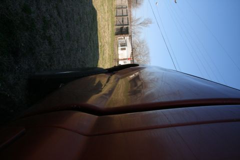 1993 Ford Bronco - The hood and windshield wiper of a brown SUV are visible from a low angle, with a clear blue sky above.