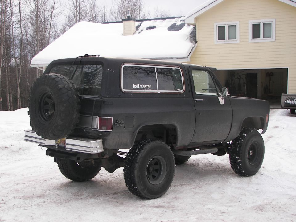 Black SUV with lifted suspension and spare tire on rear bumper, seen in snow