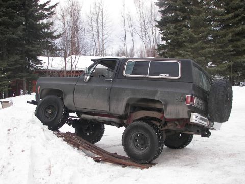 1990 Chevrolet Suburban - This lifted, dark gray SUV is positioned on a snowy ramp, its off-road capabilities and spare tire. The body style suggests a 1973-1980 mod…