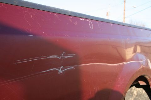 1993 Ford Bronco - Side view of a red truck's body panel, heavily scratched with white pinstripe graphics.
