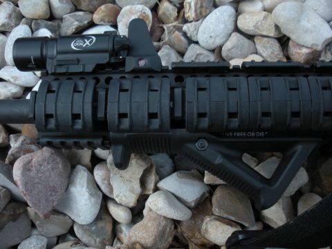 1996 Ford Bronco - A rifle with tactical accessories is shown against a backdrop of stones, with visible text on its frame.