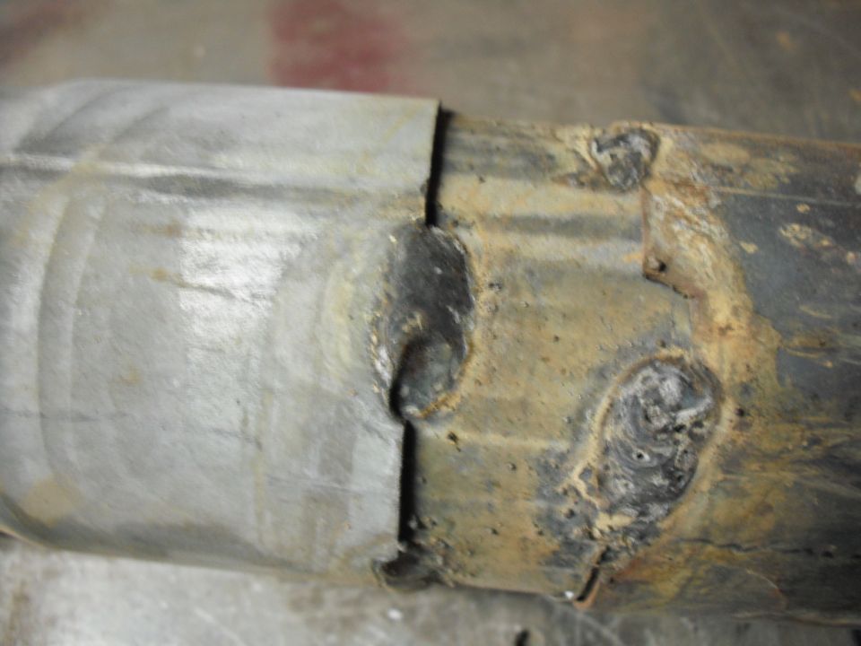 Close-up of a welded exhaust pipe section with rust and metal join
