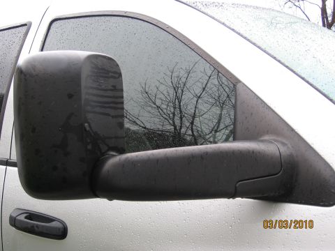 2007 Dodge 2500 - A close-up view of a black tow mirror mounted on the side of a white truck, with water droplets visible on the vehicle's surface.