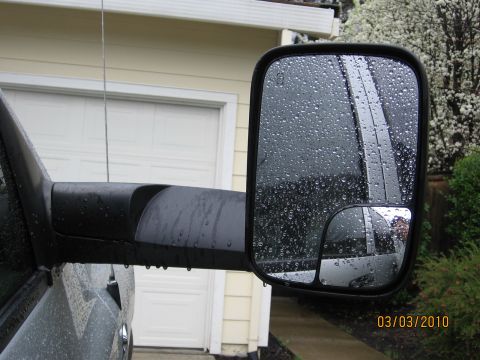 2007 Dodge 2500 - Truck's towing mirror on a rainy day, reflecting the surroundings and a garage.