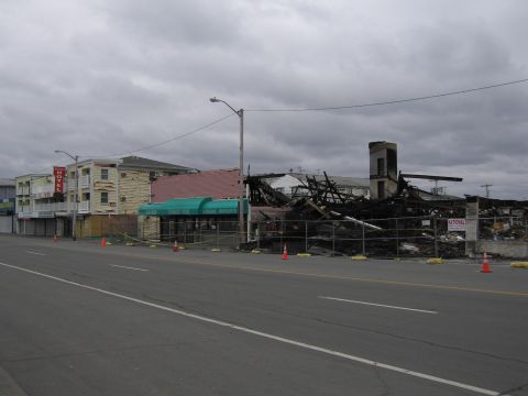 2001 Ford Crown Victoria - A building shows extensive fire damage, with debris contained by a fence and marked by traffic cones.