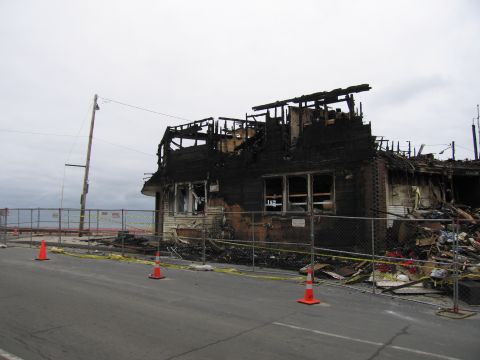 2001 Ford Crown Victoria - A building heavily damaged by fire, with debris visible behind a safety fence.