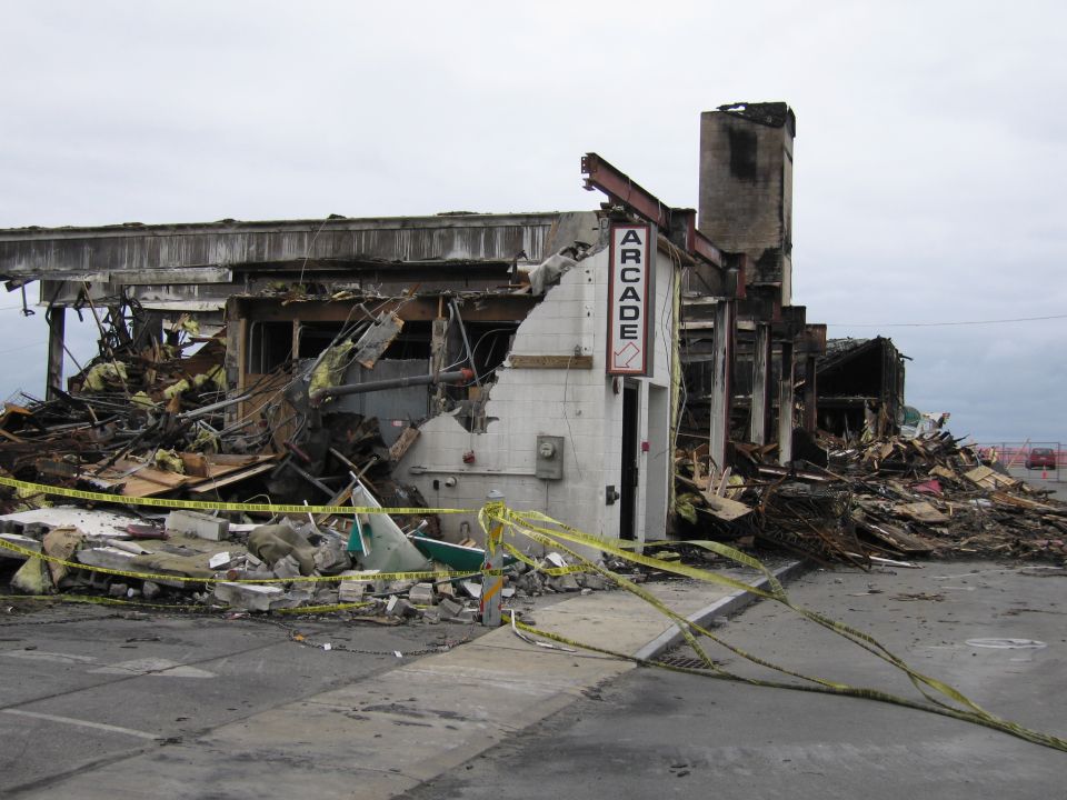 destroyed building with arcade sign, debris everywhere, caution tape
