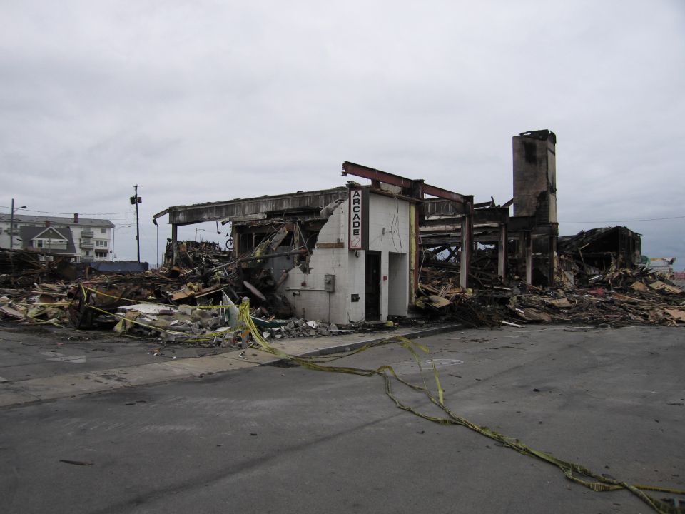 Ruined arcade building with debris and caution tape on a cloudy day