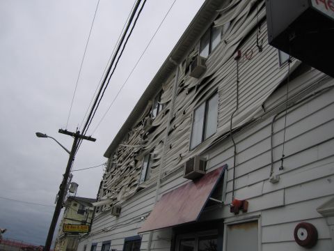 2001 Ford Crown Victoria - A building's siding is severely damaged, with large sections torn away, exposing the structure underneath. Power lines and a street lamp ar…