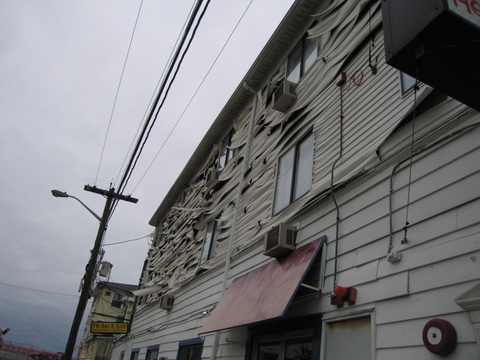 Building with siding ripped away, revealing damage and air conditioning units. Power lines and a street lamp are visible