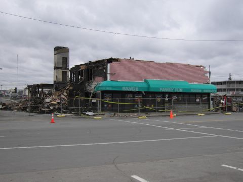 2001 Ford Crown Victoria - A building, likely a former arcade or entertainment venue, shows extensive fire damage and is cordoned off with caution tape.