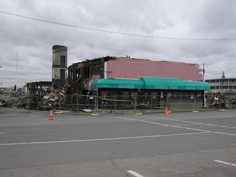 Burned-out building with a damaged roof and debris, behind a safety fence