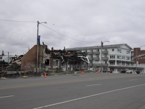 2001 Ford Crown Victoria - A white pickup truck is visible near a severely damaged building and a large hotel under a cloudy sky.