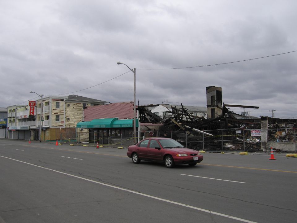 Red 2001 Ford Crown Victoria sedan driving past a fire-damaged building