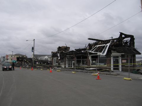 2001 Ford Crown Victoria - Fire-damaged commercial buildings line a street, with a dark SUV parked nearby.