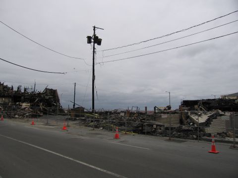 2001 Ford Crown Victoria - The aftermath of a fire shows extensive damage to buildings and debris scattered across the scene, cordoned off by a fence.