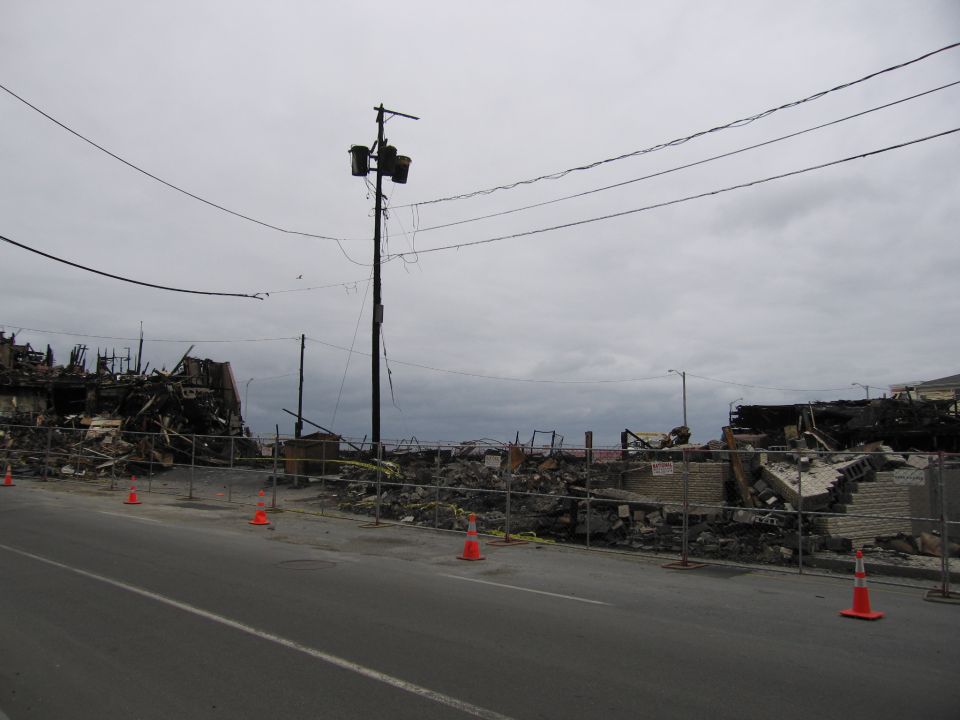 Scene of destruction after a fire with debris and damaged buildings behind a fence