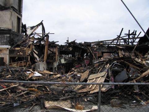 2001 Ford Crown Victoria - The aftermath of a fire shows a destroyed building with charred remains and scattered debris.