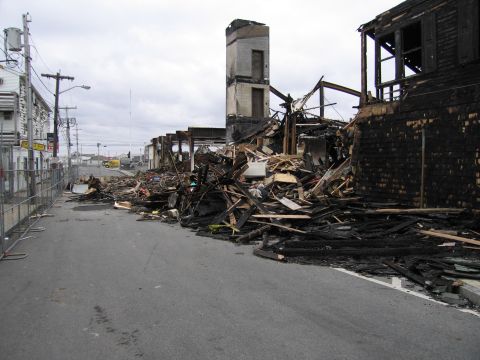 2001 Ford Crown Victoria - Scene of destruction following a fire, with damaged structures and scattered debris lining the street.