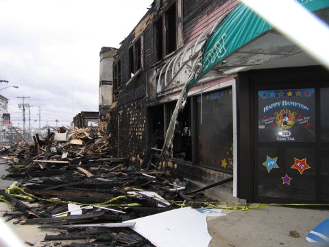 2001 Ford Crown Victoria - A building shows extensive fire damage, with debris scattered across the sidewalk and street, cordoned off by caution tape.