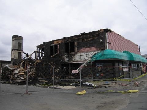 2001 Ford Crown Victoria - A building shows extensive fire damage, with a partially intact facade and a collapsed roof structure.