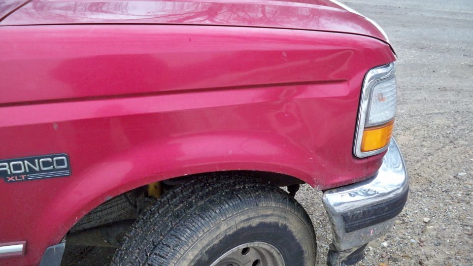 Dented front fender of a red Ford Bronco XLT