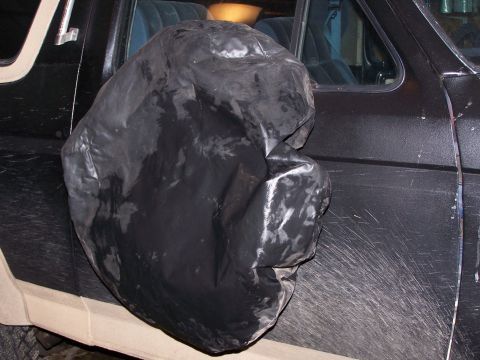 1986 Ford Bronco - A black cover obscures the spare tire on the side of a dark-colored SUV.