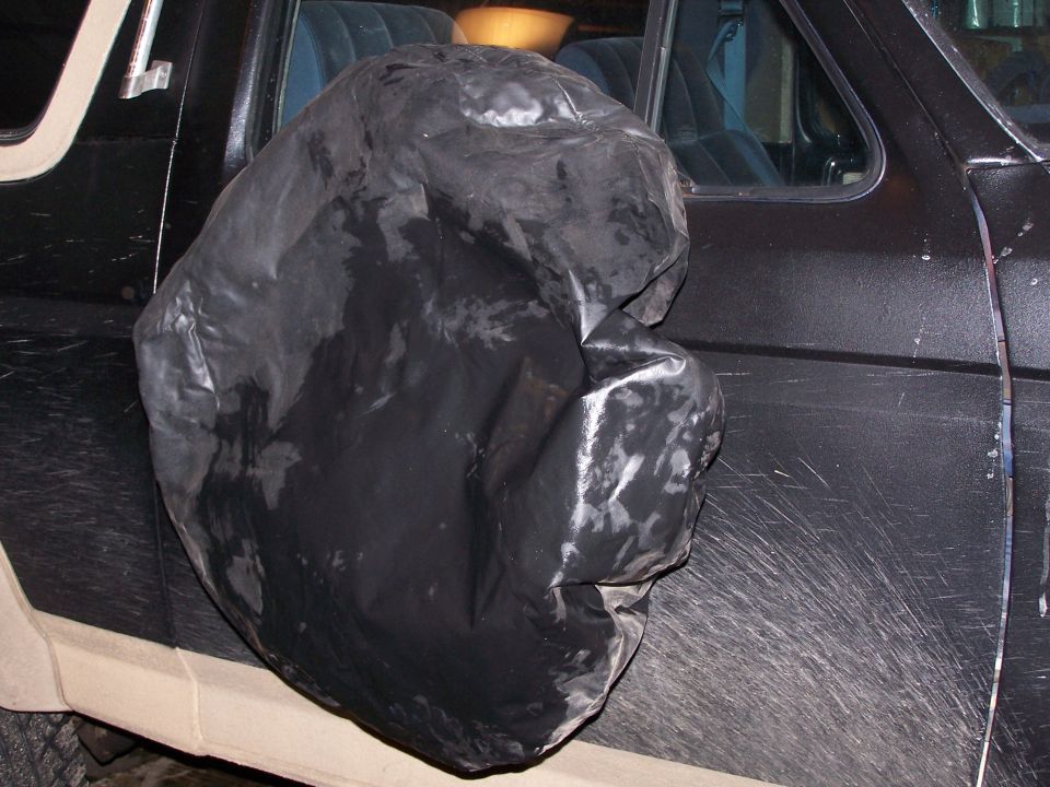 Side view of a black SUV with a large, black, crinkled cover over the spare tire. Interior seats are visible