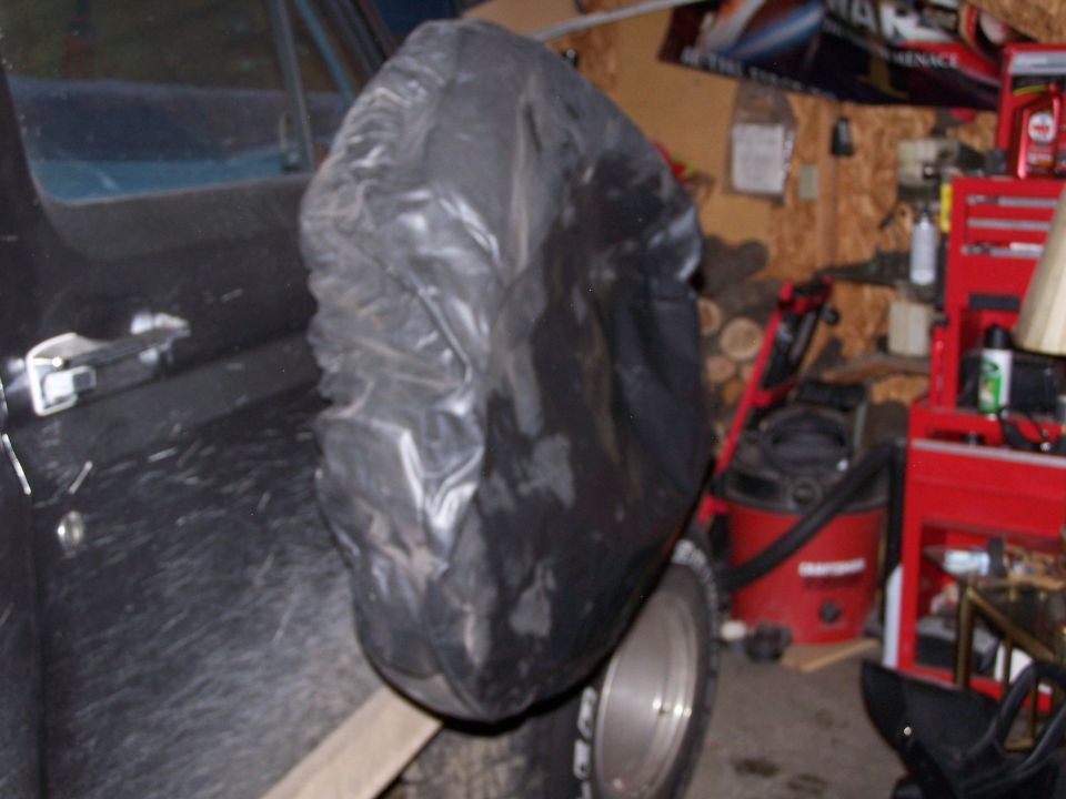 Black spare tire cover on a dark vehicle, with a silver rim visible