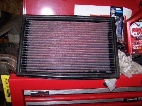 1986 Ford Bronco - A red air filter with a black frame rests on a red toolbox, with various automotive fluids and parts visible in the background.