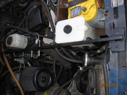 1994 Ford Bronco - Close-up view of various engine components including the battery, fluid reservoirs, and air filter assembly.