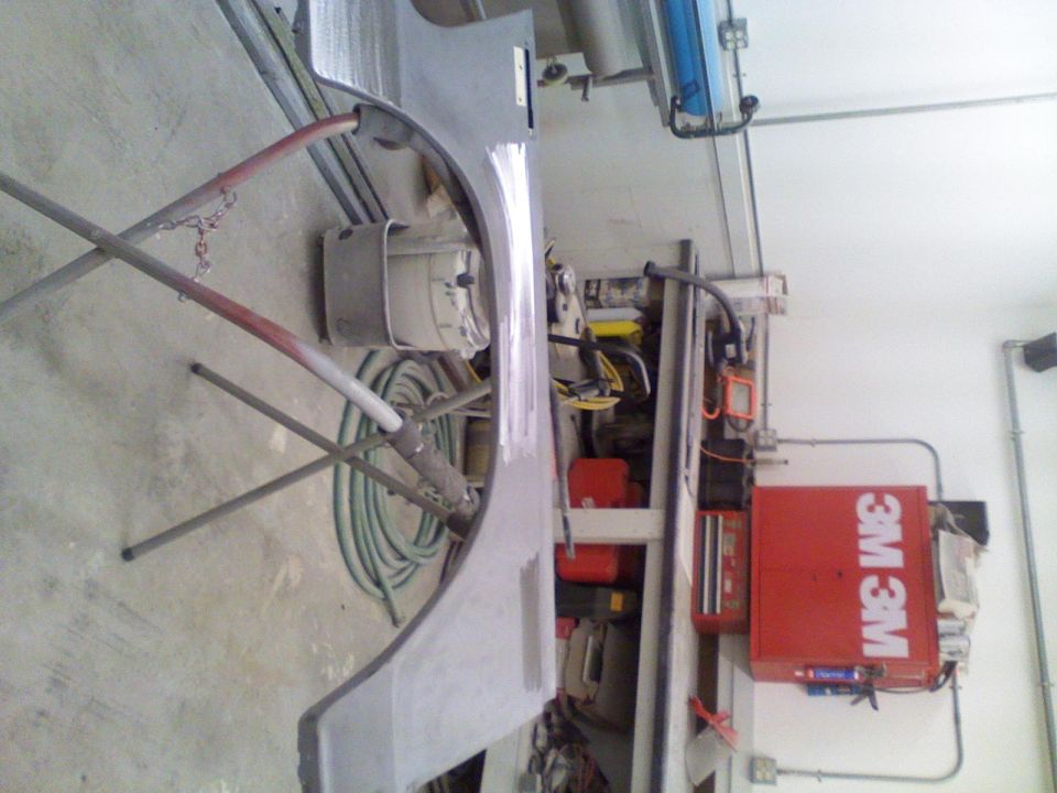 Car fender on a stand in a workshop with tools and equipment in the background. A red 3M box is visible
