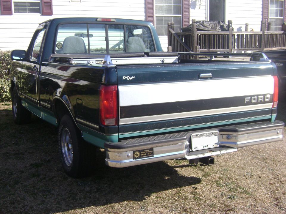 Rear 3/4 view of dark green and teal Ford F-150 pickup with chrome bumper and Georgia plate parked on grass