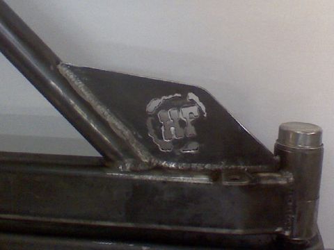 1993 Ford Bronco - Close-up of a custom metal bracket with a cut-out logo. Welded seams are visible.