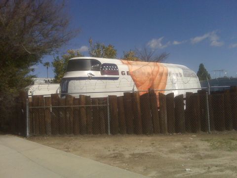 1996 Ford Bronco - A vintage trailer with patriotic decals is parked behind a wooden fence on a sunny day.