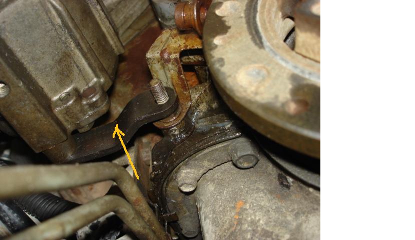 Close-up of a metal bracket with an arrow pointing to it, attached to an engine component